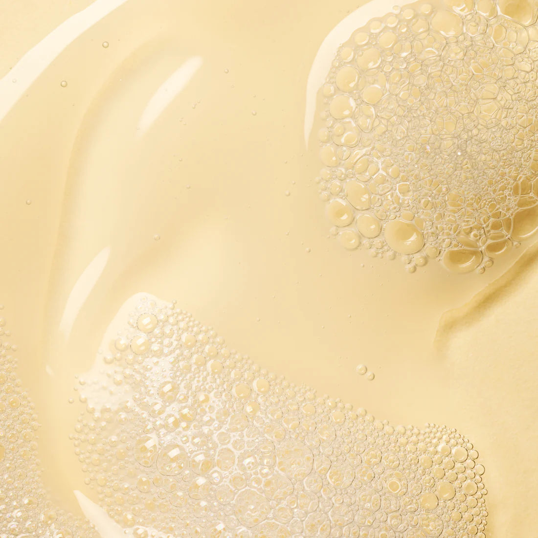 Close-up of clear, pale yellow Lumene Nordic-C Strength & Shine Shampoo, with clusters of small, shiny bubbles giving the liquid a textured and glossy look.