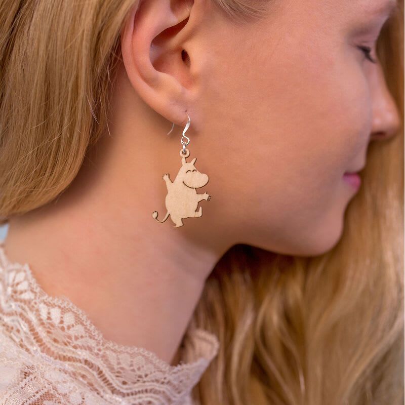 A woman with long blonde hair wears a lace top and light wooden earrings shaped like cartoon animalsâshowcasing playful Coruu Moomin Wooden Earrings inspired by Nordic jewelry.