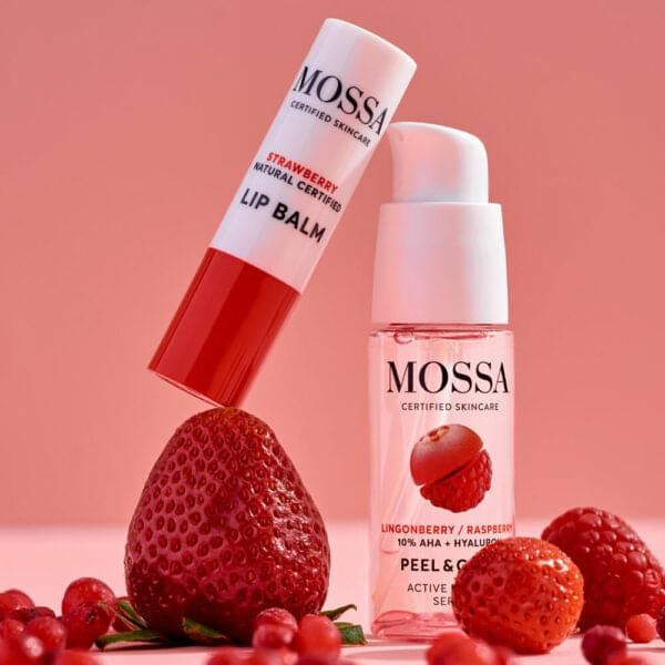 The Mossa Berry Kiss Gift Set featuring hydrating lip balm and overnight peeling serum is displayed among strawberries, raspberries, and lingonberries against a pink background.