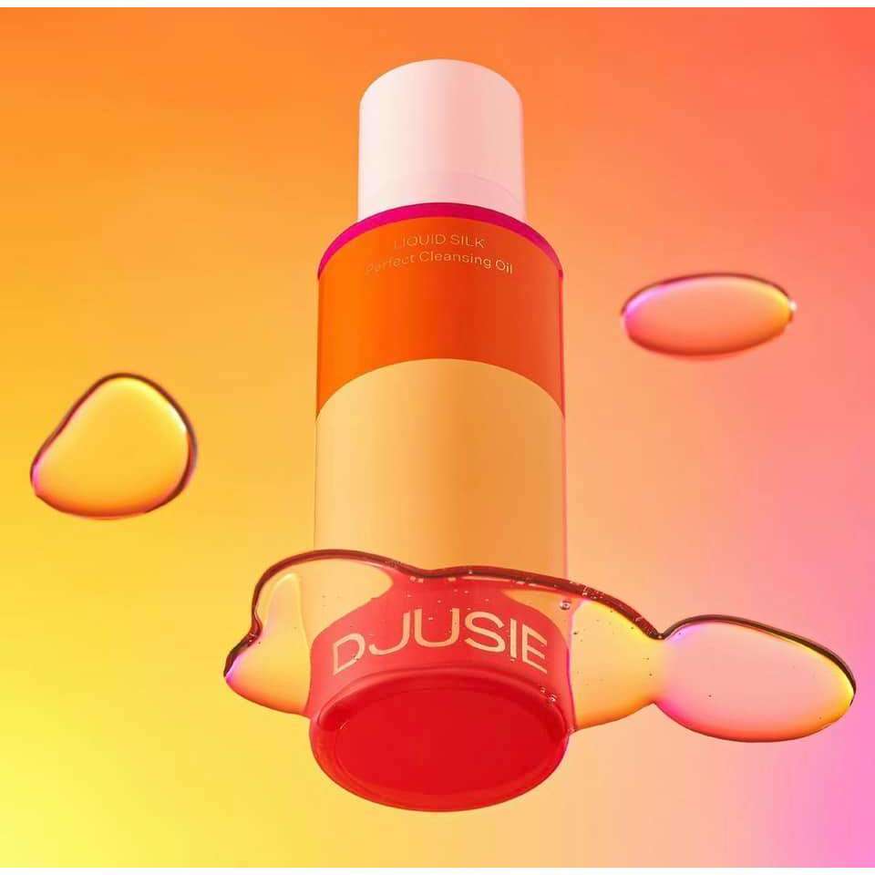 A vibrant orange and yellow bottle of Djusie Liquid Silk Perfect Cleansing Oil by Djusie appears to float above a peach-pink background, surrounded by glistening droplets—ideal for removing water-resistant makeup.