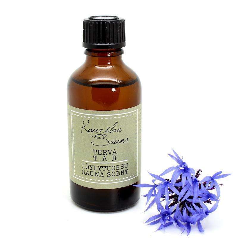 A brown glass bottle of Kaurilan Sauna Tar Sauna Scent by Kaurilan Sauna is placed beside a cluster of purple flowers on a white background.