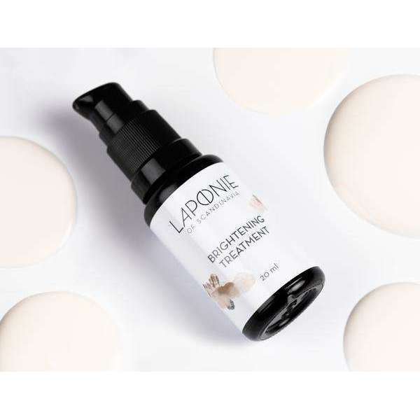 A bottle of Laponie of Scandinavia Clarifying Treatment Serum for sensitive skin rests on a white surface with creamy lotion spots. It features a black pump and a white label with black text and subtle floral accents.