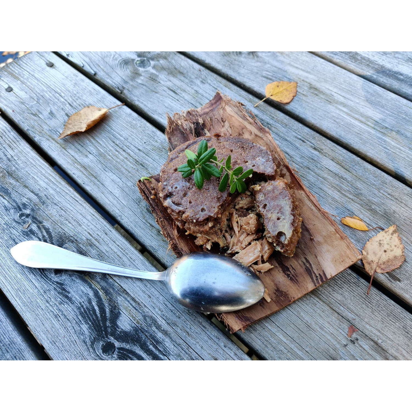 A rustic Finnish treat, Pielisen Kala Finnish Fish Pasty by Pielisen Kala is served on bark with a silver spoon and autumn leaves, capturing the authentic charm of traditional Muikkukukko flatbread and fish.