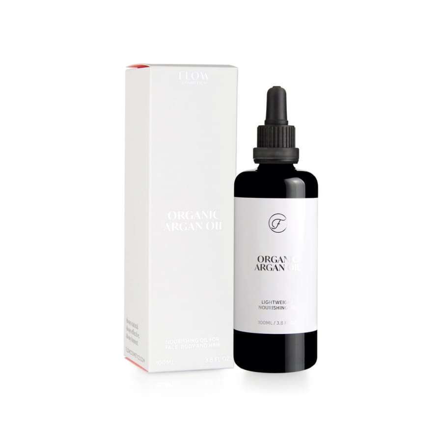 A black bottle of FLOW Cosmetics Organic Argan Oil with a dropper cap sits beside its matching white minimalist box. The label features "Organic Argan Oil" and "Lightweight Nourishment," ideal for sensitive skin. Brand: Flow Cosmetics.