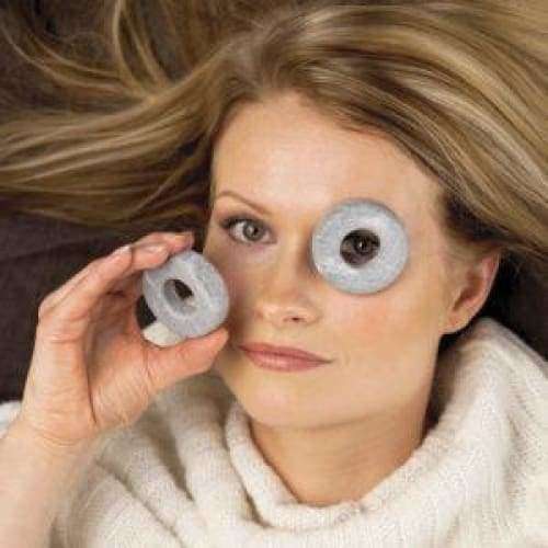 A woman with long blonde hair and a calm expression wears a white sweater while playfully holding Hukka Orbits Eye Stones from Hukka over her eyes like glasses.