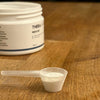 A small plastic scoop filled with white THERA Nordic Rezcue Drink Powder sits on a wooden surface, hinting at gut healing benefits, with a partially visible THERA Nordic container in the background.