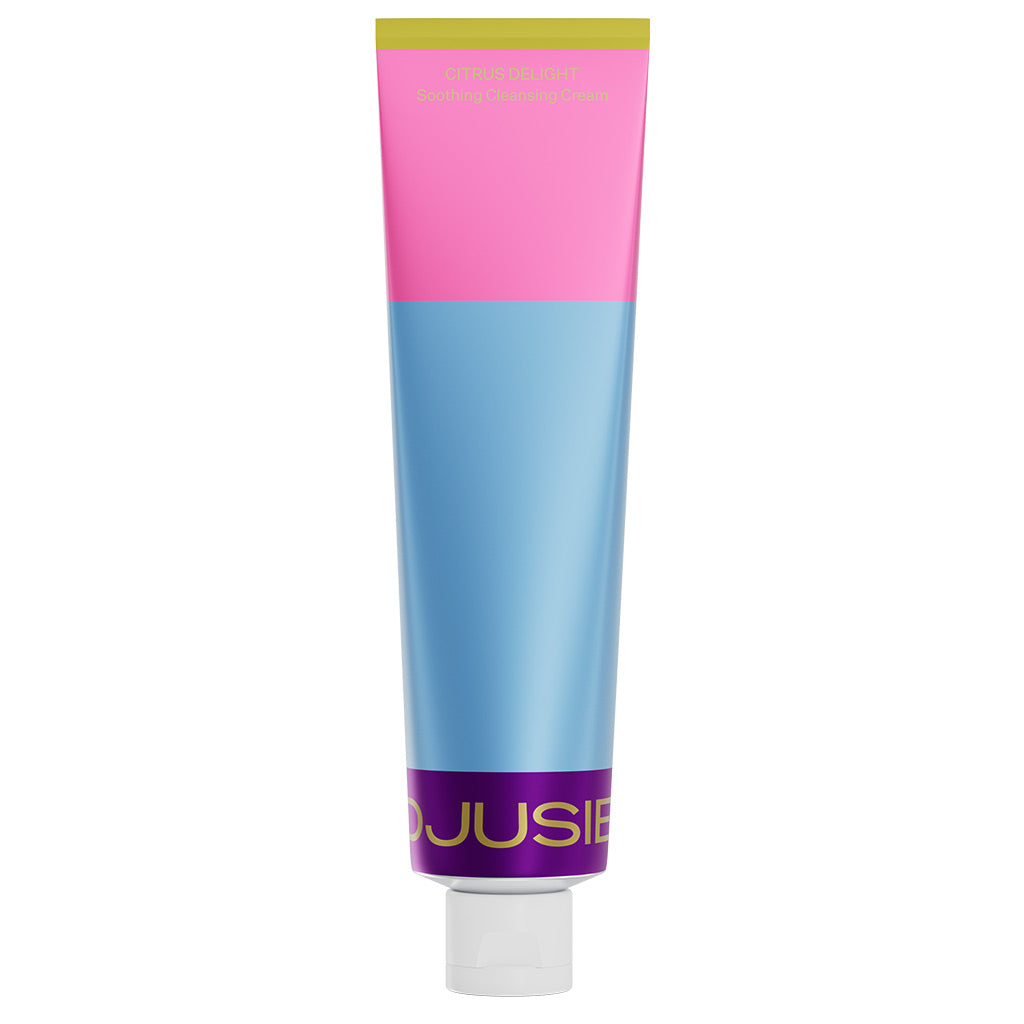 A tube with a pink, blue, and purple color block design stands upright with a white cap. “Djusie” is partially visible near the bottom—perfect for your deeply nourishing skincare routine with the Djusie Juicy Skin Box.