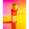 A bottle of Djusie Liquid Silk Perfect Cleansing Oil stands upright against a vibrant yellow, orange, and pink gradient. The sleek bottle features a yellow cap and bold white branding, effortlessly removing water-resistant makeup.