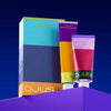 Two vibrant cosmetic tubes labeled Djusie stand upright with the Djusie Dream Team Box, set against a blue and purple backdrop, showcasing nourishing night treatment and moisturizing fluid with bold color blocks.