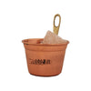 The Emendo Stove Cup & Himalaya Salt set by Emendo features a copper cup labeled SAUNA, holding a large chunk of Himalayan salt to enrich sauna steam, with a brass handle that has a circular opening at the top.