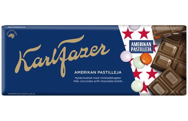 A Fazer American Lentils Milk Chocolate bar wrapper with blue and gold branding, red stars, chocolate pieces, and colorful candy-coated lentils. Text in Finnish, Swedish, and English describes this tasty treat.