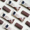Foodin Clean & Real Protein Bar Crispy Chocolate Bliss bars and wrappers are laid out diagonally on a light surface. Each bar from Foodin is high in protein and contains no added sugar, making it a wholesome treat.