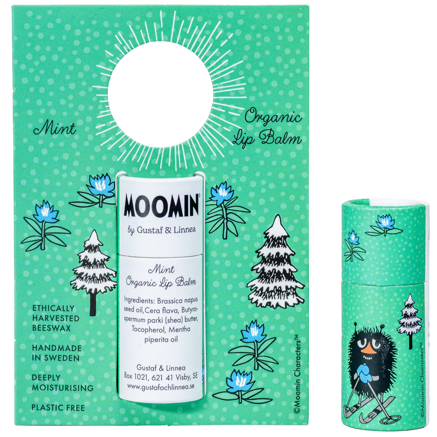 A green package and tube of Gustaf & Linnea Moomin Lipbalm Stinky features trees, flowers, and a Moomin character. Swedish-made and ethically sourced, it highlights natural ingredients like organic mint and beeswax.