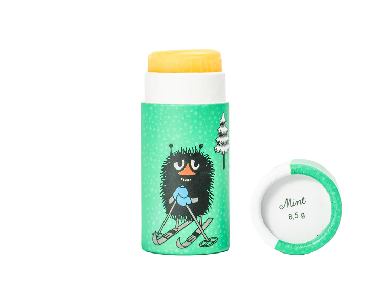 The Gustaf & Linnea Moomin Lipbalm Stinky is an eco-friendly stick with a green wrapper, two tree illustrations, and features the black Moomin character Stinky on skis. Made with Swedish beeswax; cap reads Mint 8.5 g.