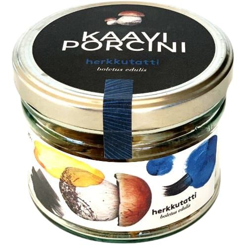 A glass jar with a gold lid labeled Kaavi Porcini Dried Porcini by Kaavi Porcini. The label displays painted Finnish porcini mushrooms and colorful blue, yellow, and black brushstrokes.
