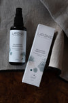 A bottle and box of Laponie of Scandinavia Balancing Essence Mist from Laponie of Scandinavia, a hydrating toner and face mist for sensitive skin, are shown on a grey fabric surface with a brown wooden edge.