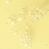 A clear glass dropper rests on a pale yellow surface with clusters of transparent bubbles, reflecting the refreshing purity of Lumene Nordic-C Glow Boost Essence by Lumene and its radiant vitamin C benefits.
