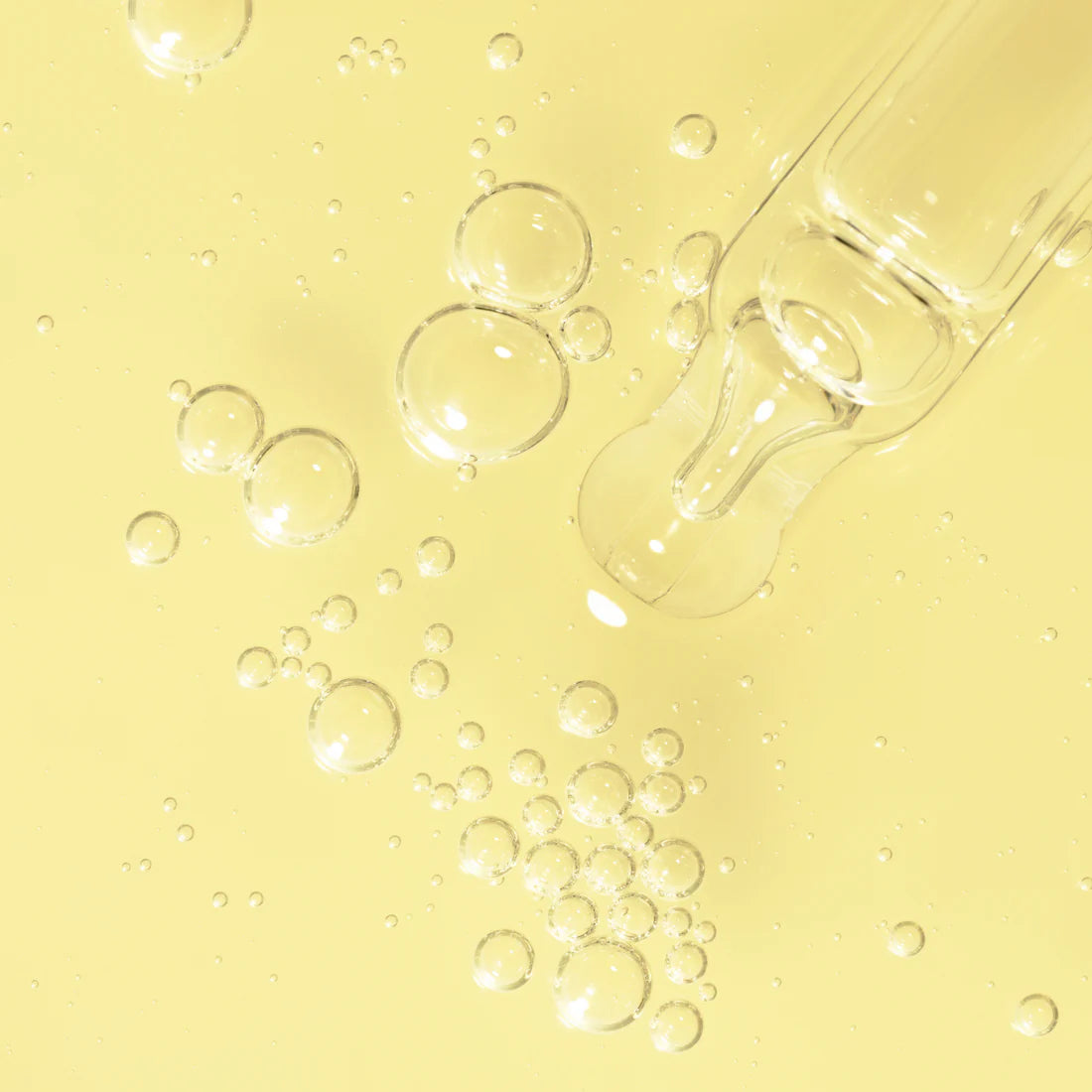 A clear glass dropper rests on a pale yellow surface with clusters of transparent bubbles, reflecting the refreshing purity of Lumene Nordic-C Glow Boost Essence by Lumene and its radiant vitamin C benefits.