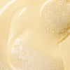 Close-up of clear, pale yellow Lumene Nordic-C Strength & Shine Shampoo, with clusters of small, shiny bubbles giving the liquid a textured and glossy look.