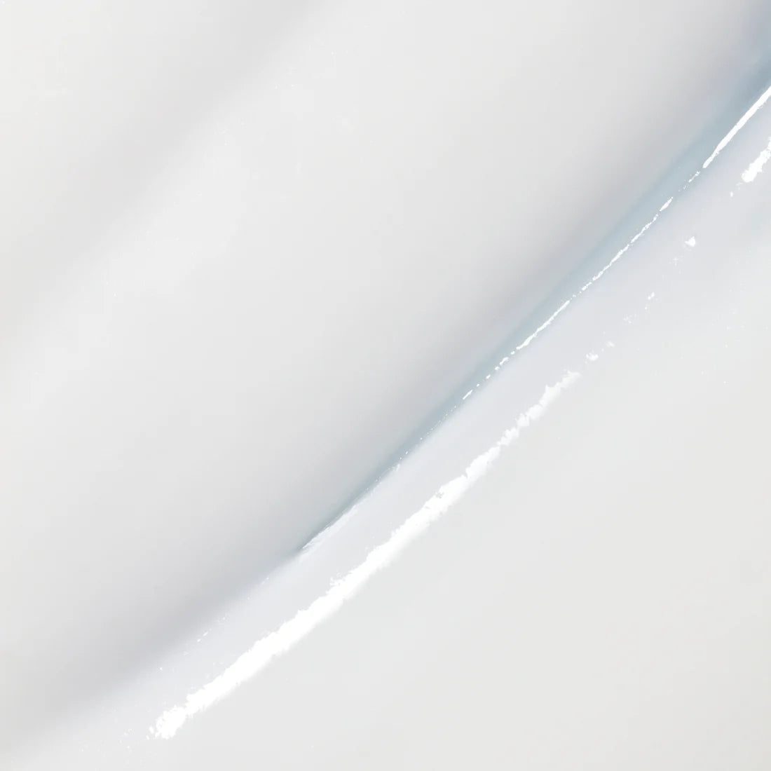 Close-up of a smooth, glossy white surface with a diagonal crease, reflecting the gentle makeup removal experience of Lumene Nordic Hydra Oat Milk Oil Cleanser for sensitive skin, with subtle shadow and shine.