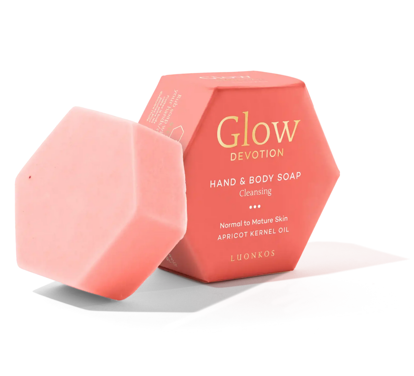 A pink hexagonal bar of Luonkos Glow Devotion Hand & Body Soap stands beside its matching box, featuring apricot kernel oil. This natural vegan soap is designed for normal to mature skin.