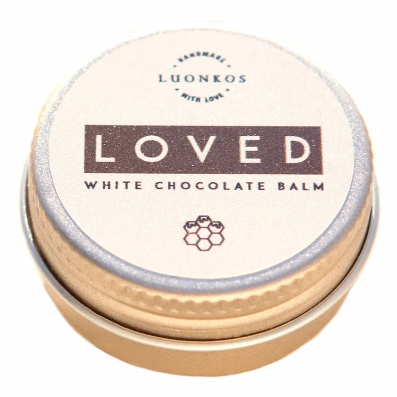 A small round tin labeled Luonkos Loved White Chocolate Multipurpose Lip Balm features minimalist design, a honeycomb symbol, beige lid with dark brown lettering, and is handmade in Finland.