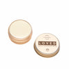 Two small round tins, one closed and one open to reveal a pale balm inside. The closed tin is labeled Luonkos Loved White Chocolate Multipurpose Lip Balm—a natural, handmade product from Finland with simple black and gold design.