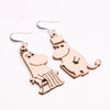Coruu Moomin Wooden Earrings by Coruu feature charming cartoon hippos—one with a skirt and necklace, the other with a top hat and cane—crafted from wood with black line details and finished with metal hooks for easy Nordic-inspired styling.