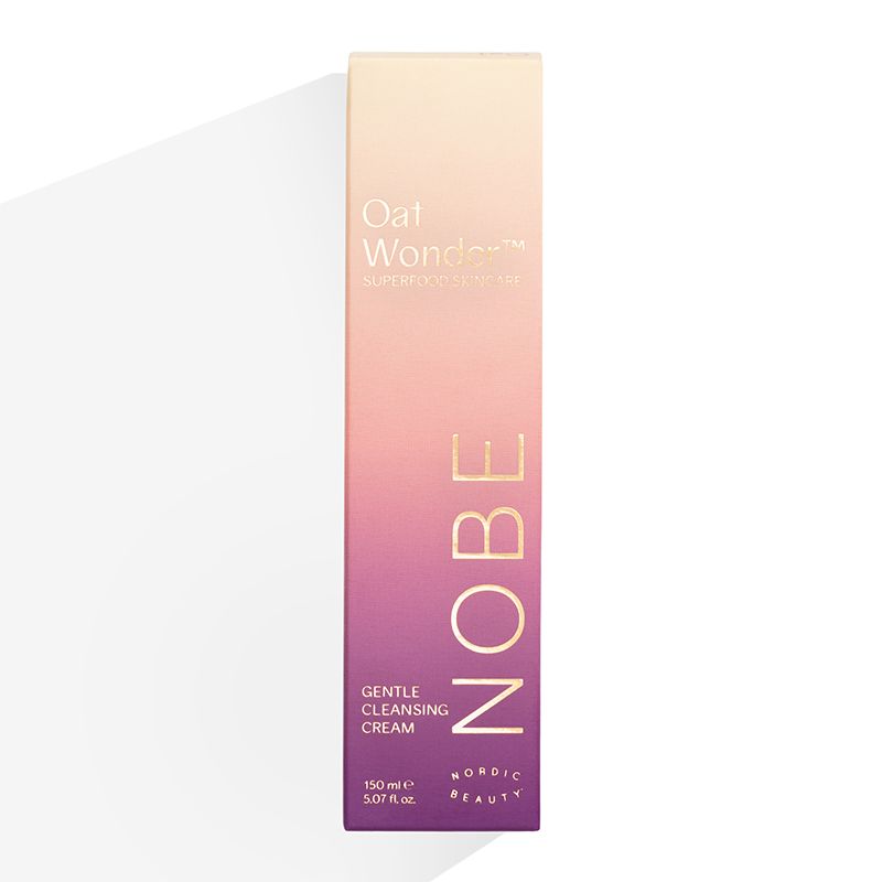 A rectangular box of NOBE Nordic Beauty’s Oat Wonder® Gentle Cleansing Cream, a creamy facial cleanser with Fazer Oat Oil, features a pink and purple gradient and gold text, displayed upright against a white background.