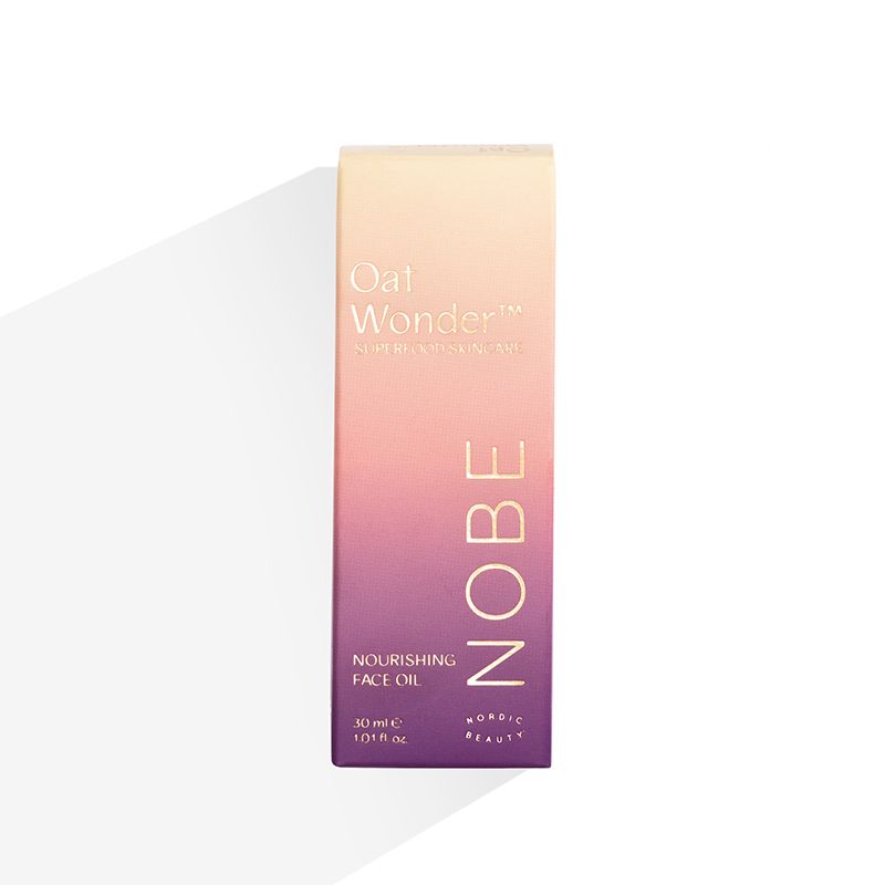 A rectangular box of NOBE Oat Wonder® Nourishing Face Oil by NOBE Nordic Beauty, featuring a gradient peach to purple design with gold text, stands upright on a white background with a light shadow.