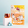 A glass mug of tea rests on a white block beside the Nordqvist Moomin Advent Tea Calendar and three blue boxes with white hearts, all set against a light blue background—ideal for enjoying a cozy vegan tea selection from Nordqvist.