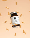 A brown glass bottle labeled Puhdistamo Multivitamin with a silver lid is surrounded by yellow capsules, showcasing Puhdistamo’s multivitamin with active B-vitamins and immune support benefits against a beige background.