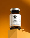 A brown glass jar of Puhdistamo Multivitamin by Puhdistamo sits on a yellow block against an orange gradient background, with a wooden spoon beside it.