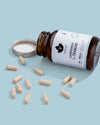 A brown bottle labeled Puhdistamo Natural L-Theanine by Puhdistamo lies on its side with the lid off, spilling beige L-Theanine capsules onto a light blue surface, evoking a sense of calm focus and stress relief.