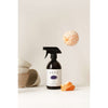 A dark SEES Company spray bottle labeled SEES Dishwashing Liquid stands upright by a peeled orange and ceramic bowls, with a whole mandarin floating above, highlighting our biodegradable, eco-friendly dish soap against a neutral background.