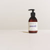 A brown pump bottle of SEES Company’s SEES Hand & Body Lotion with organic birch sap rests on a light surface against an off-white background.