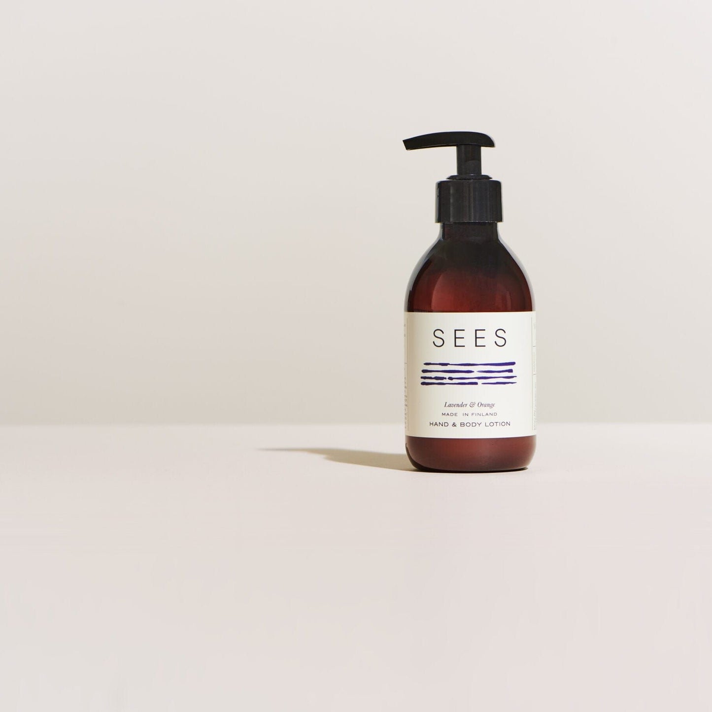 A brown pump bottle of SEES Company’s SEES Hand & Body Lotion with organic birch sap rests on a light surface against an off-white background.