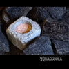 The Kiuassuola Sauna Salt ILMARI Starter Pack features a pinkish natural sauna salt block in a square stone container, surrounded by dark stones—perfect for enhancing your wellness ritual.