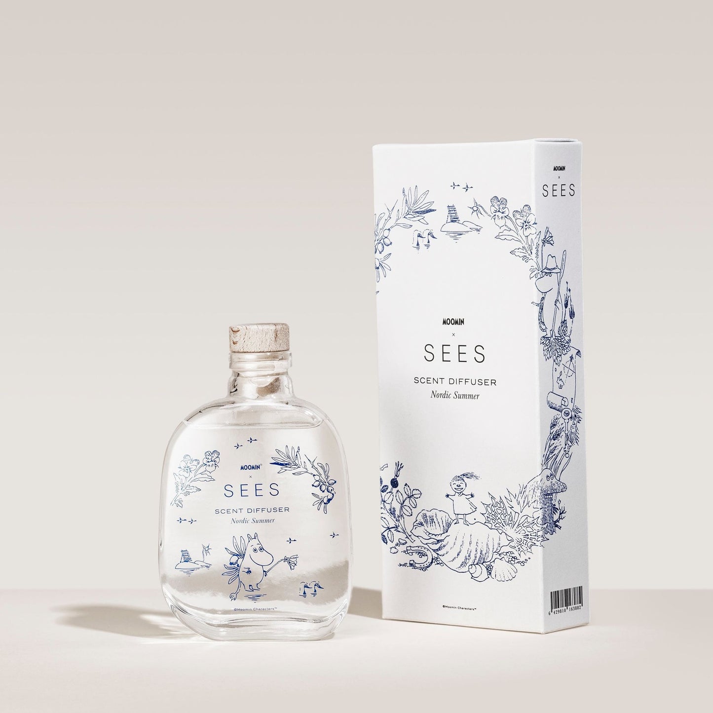 The SEES Company SEES x Moomin Room Diffuser Nordic Summer, a biodegradable diffuser in a clear glass bottle with cork, stands by a white box adorned with blue botanicals and branding—evoking a refreshing Nordic summer scent.