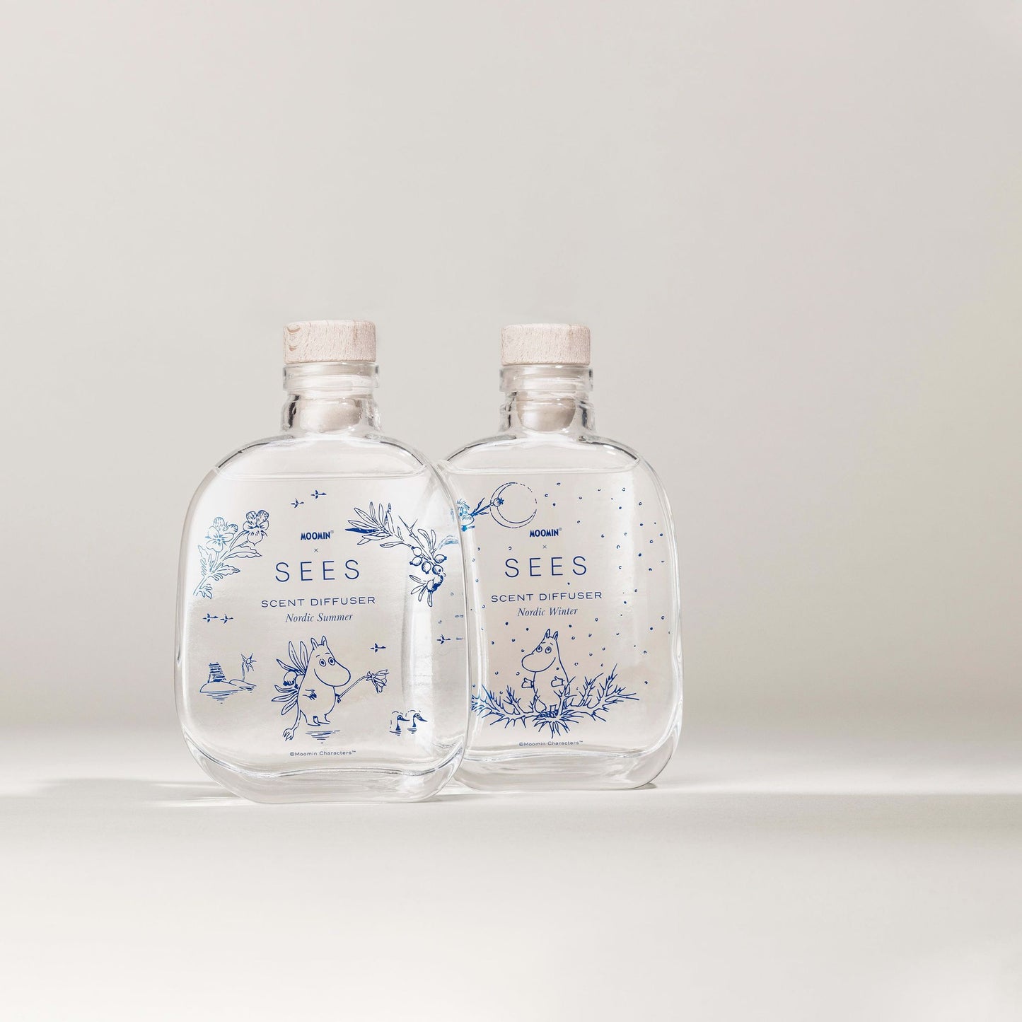 Two clear glass SEES x Moomin Room Diffuser Nordic Summer bottles by SEES Company, each with a cork stopper and blue floral and character designs—an enchanting Moomin-inspired room diffuser evoking Nordic summer.