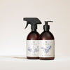 Two brown bottles with white labels from SEES Company; one is SEES x Moomin Dish Wash Spray with a spray nozzle and biodegradable dishwashing liquid, the other is Hand Wash with a pump. Both feature blue botanical illustrations on a neutral background.