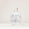 A clear glass bottle with a cork stopper labeled SEES x Moomin Room Diffuser Nordic Summer by SEES Company, featuring blue floral designs, leaves, and a small Moomin character, sits on a plain light background.