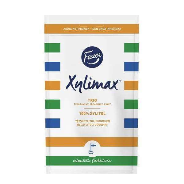A white Fazer Xylimax Trio Full Xylitol Chewing Gum pack by Fazer features blue, green, orange, and yellow stripes. It promotes 100% xylitol for dental health and includes peppermint, spearmint, and fruit flavors.