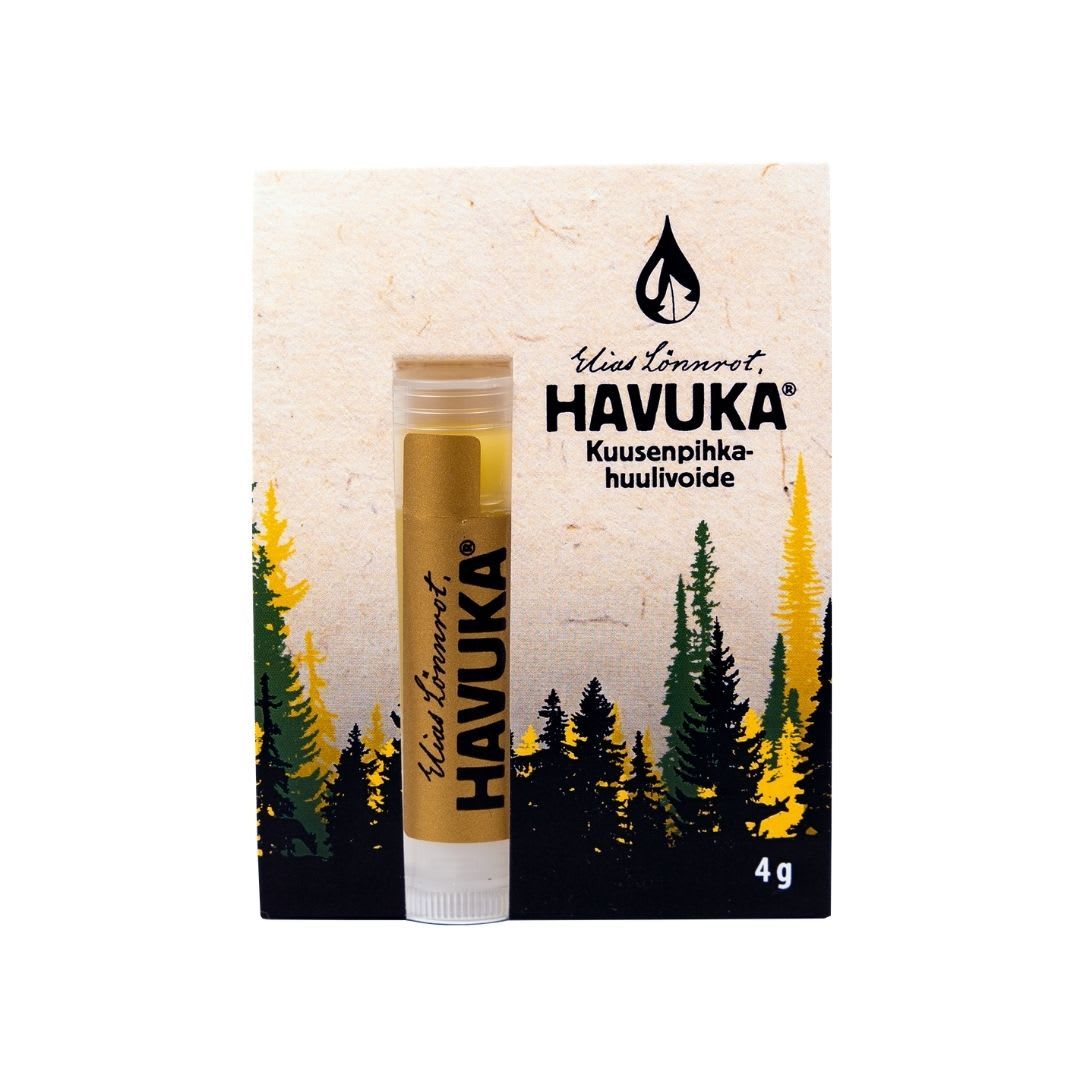 A gold tube of Havuka Spruce Resin Lip Balm sits before its cardboard box, which displays illustrated evergreen trees, Finnish text, a black droplet icon, and notes a weight of 4g.
