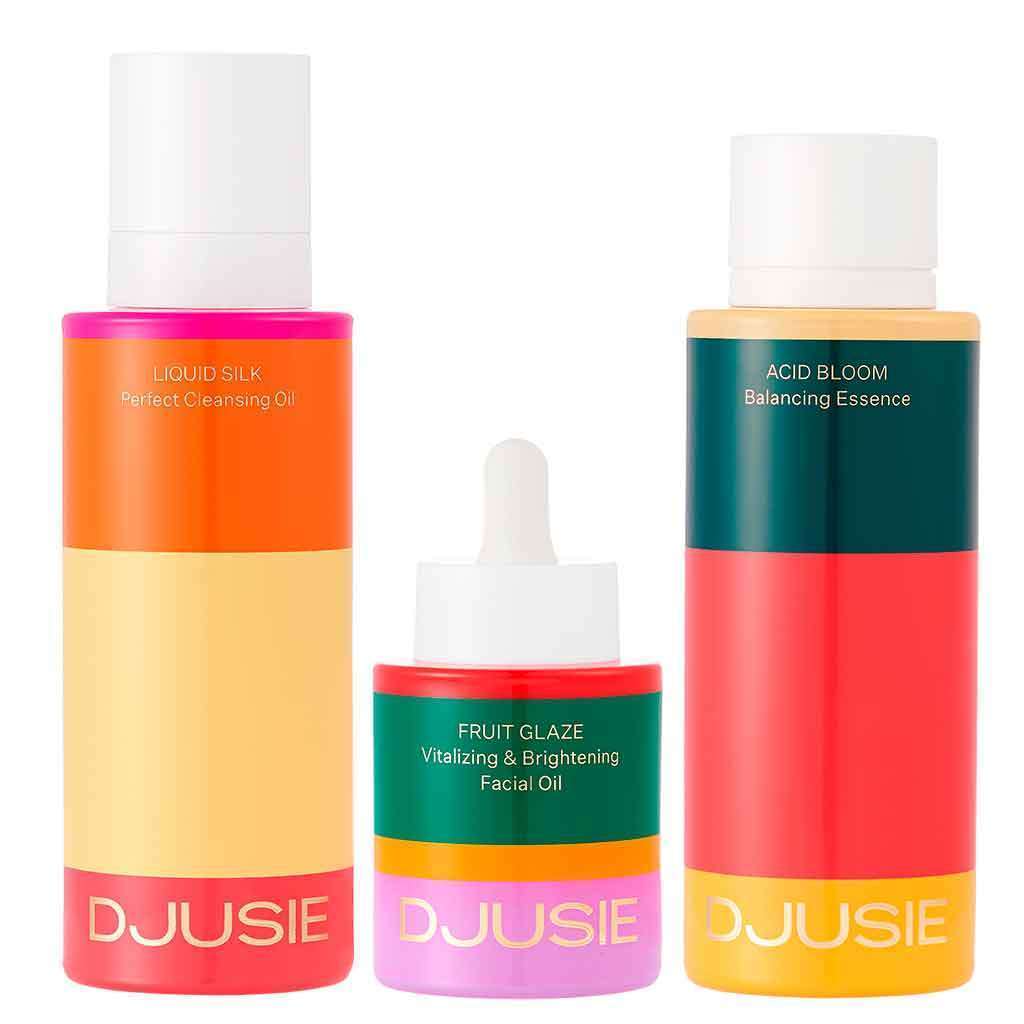 The Djusie Full Bloom Box Skincare Set features three colorful products: a cleansing oil, a facial oil with dropper, and a balancing essence—each with bold color block labels.