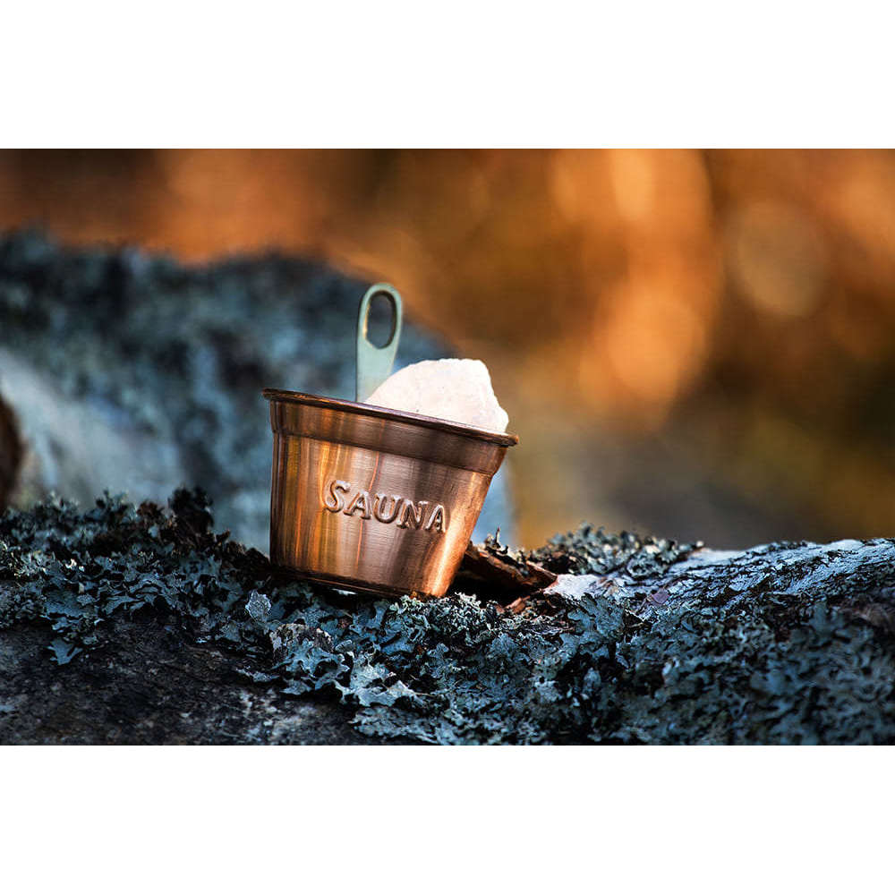 The Emendo Stove Cup & Himalaya Salt, from Emendo, sits atop a mossy rock—ideal for creating soothing sauna steam and enjoying natural allergy relief in a warm, tranquil setting.