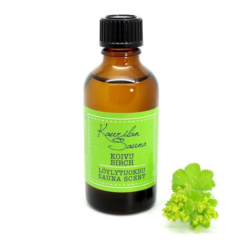 A small amber glass bottle with a black cap labeled Kaurilan Sauna Birch Sauna Scent sits beside a green birch leaf and flower cluster, showcasing its fresh birch scent vegan sauna fragrance on a white background.