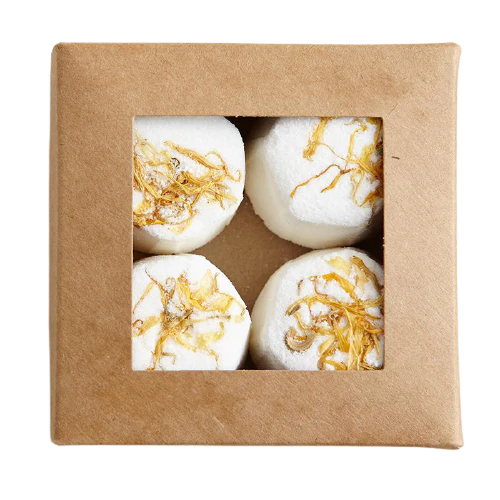 A square box with a window displays Kaurilan Sauna Lemongrass Footbath—handmade in Helsinki for a unique artisan touch. Four round white footbaths are arranged in a 2x2 grid, topped with thin golden strands.