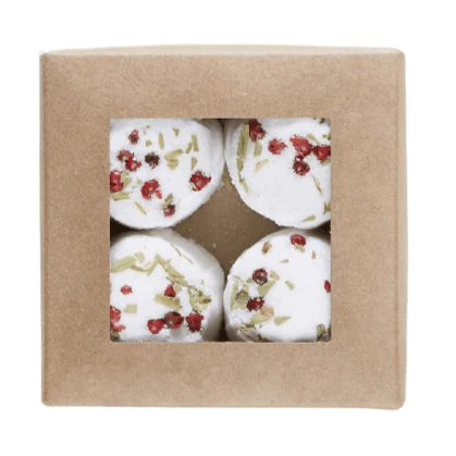 A brown cardboard box with a clear window displays four round Kaurilan Sauna Peppermint Footbath bombs, each topped with dried herbs and petals—handmade in Helsinki by Kaurilan Sauna using natural cosmetics.