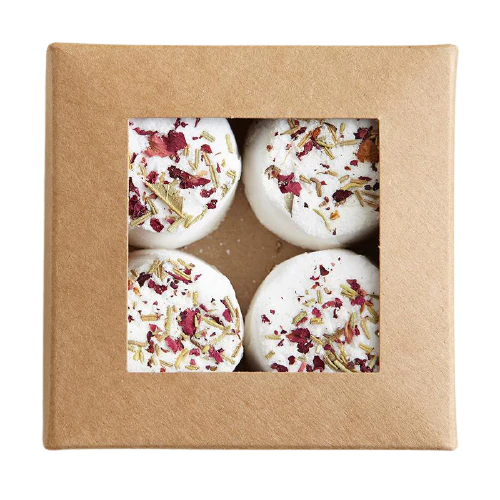 A brown cardboard box with a clear window showcases four round Kaurilan Sauna Rosemary Footbath bombs, handmade in Helsinki from natural cosmetics and topped with dried flower petals and herbs.
